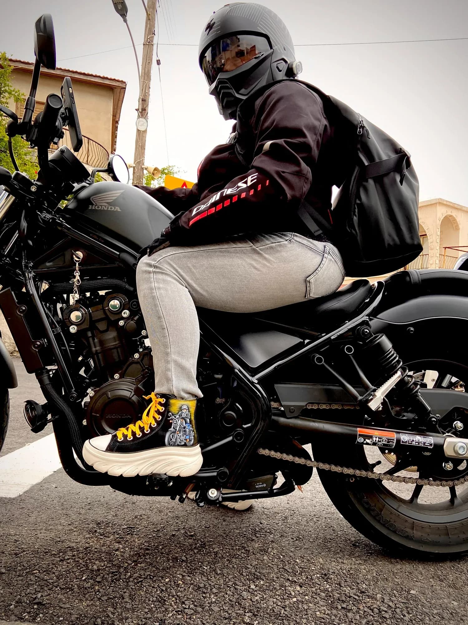 Motorcyclist in a helmet wearing hand-painted high-tops, seated on a motorbike