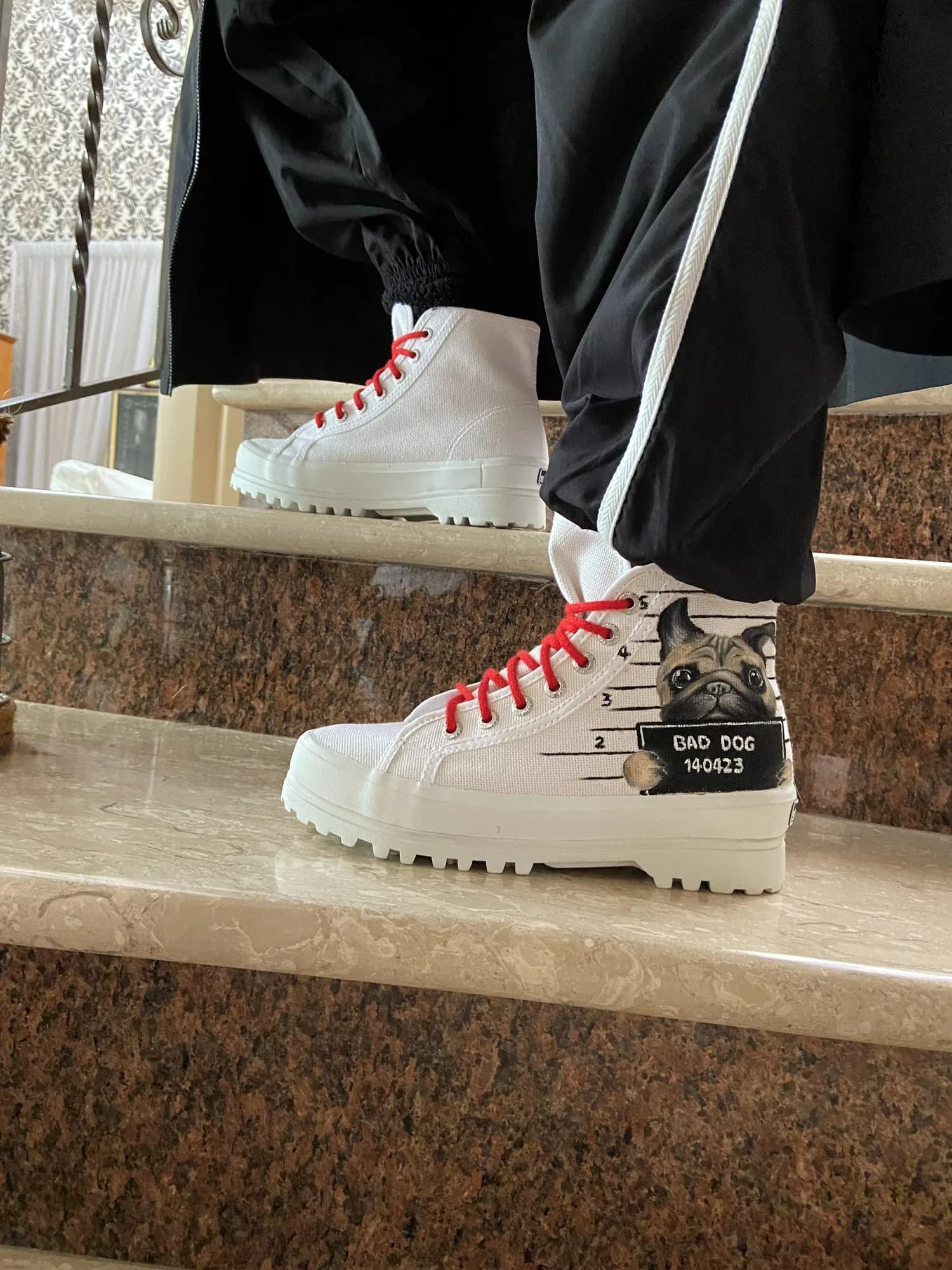 White platform boots with red laces and a dog hand-painted on a name-tag sign, worn on stairs