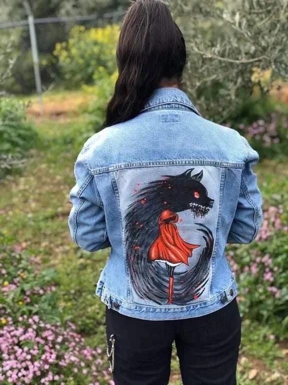 Denim jacket hand-painted with a wolf and Little Red Riding Hood, worn in a garden