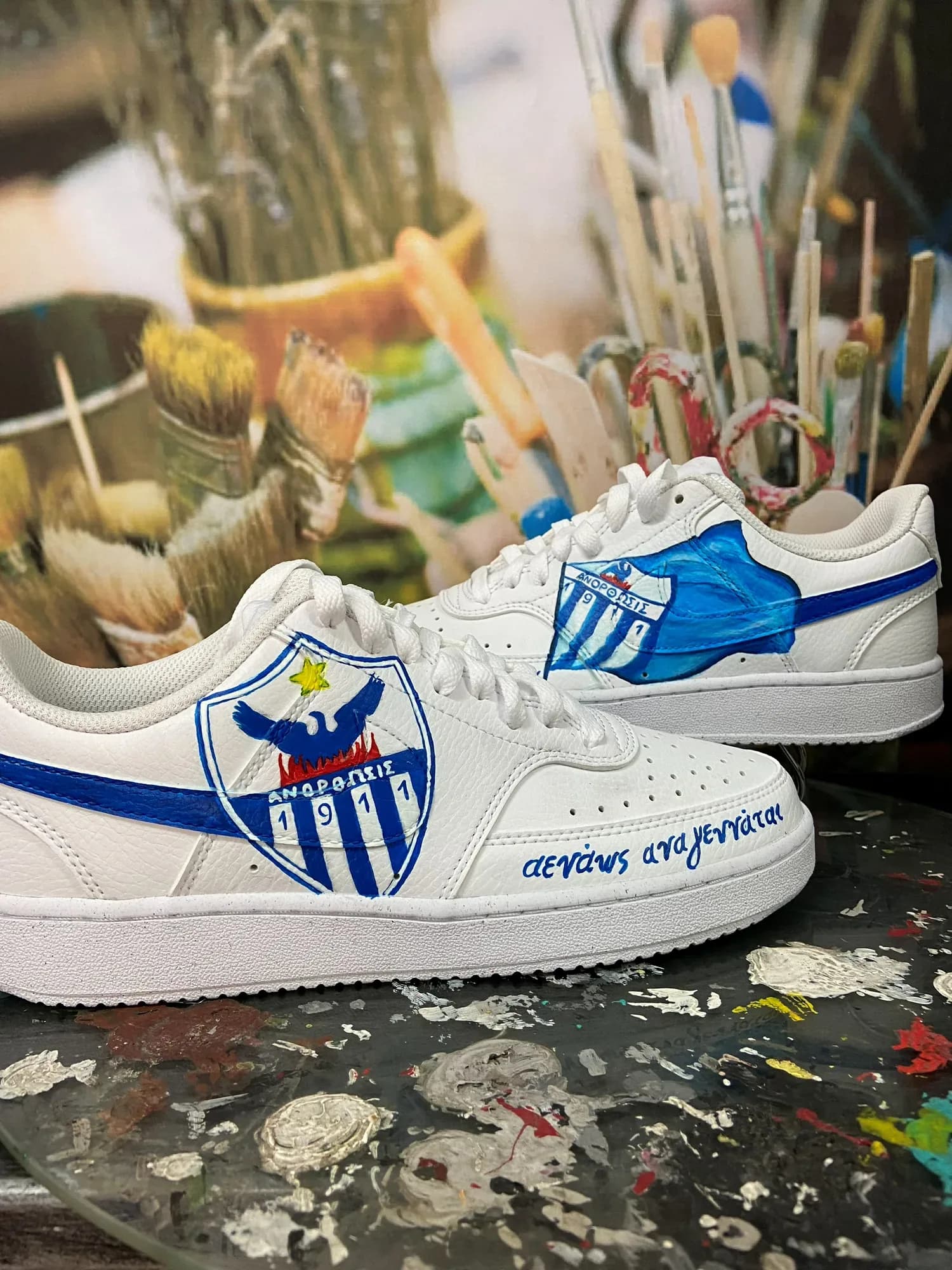 White sneakers hand-painted with the Anorthosis badge with its phoenix and a blue swoosh
