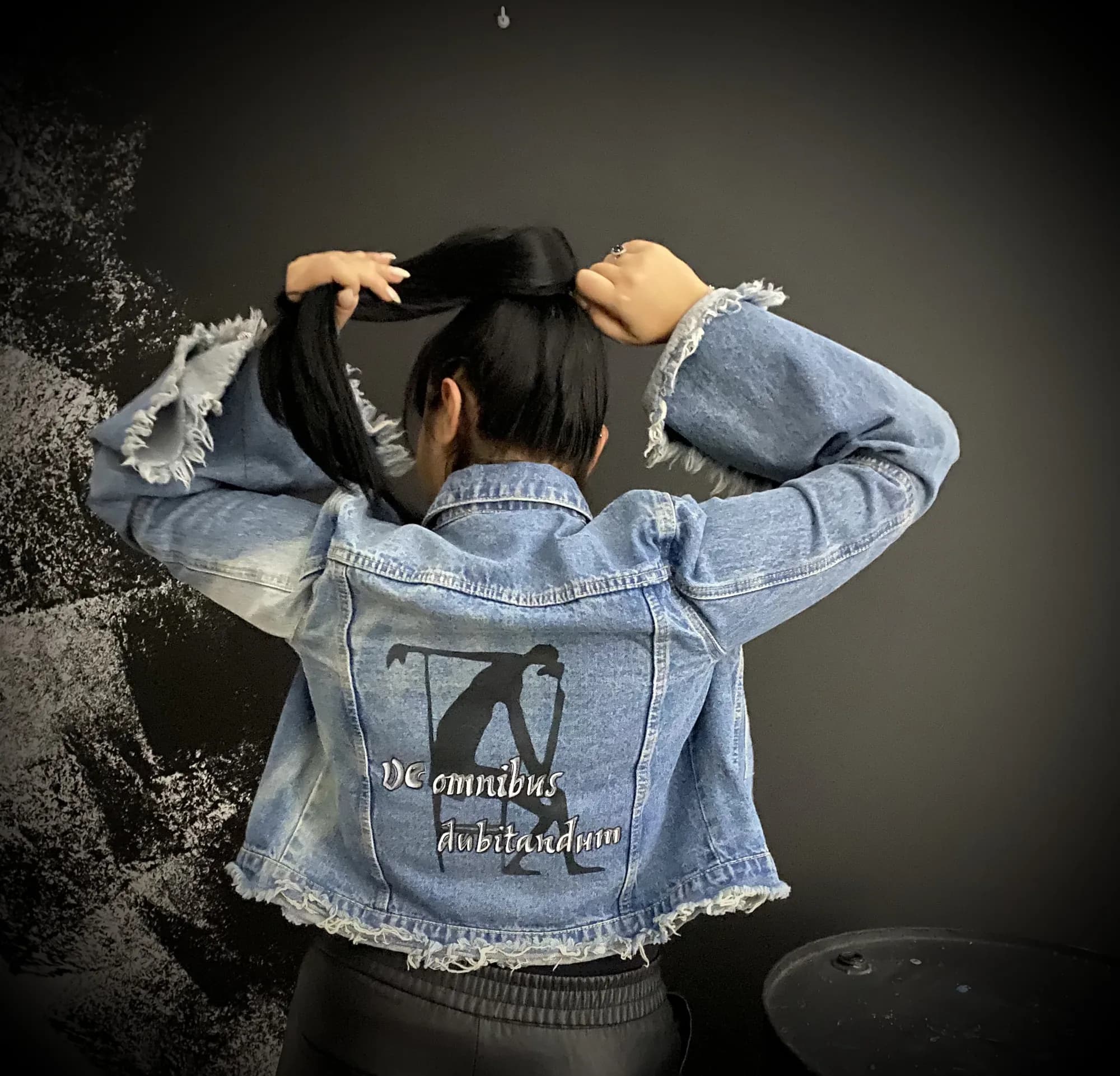Frayed denim jacket hand-painted on the back with a black figure and a Latin phrase