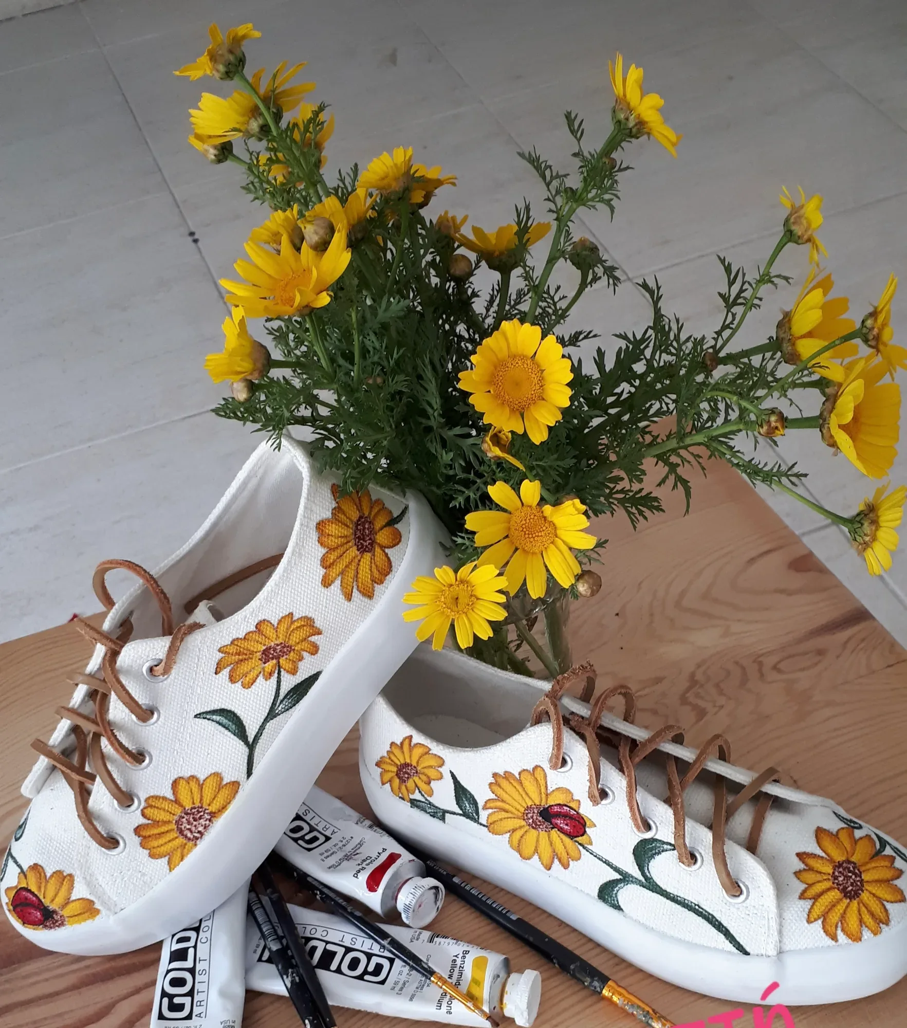 White sneakers hand-painted with sunflowers next to fresh flowers